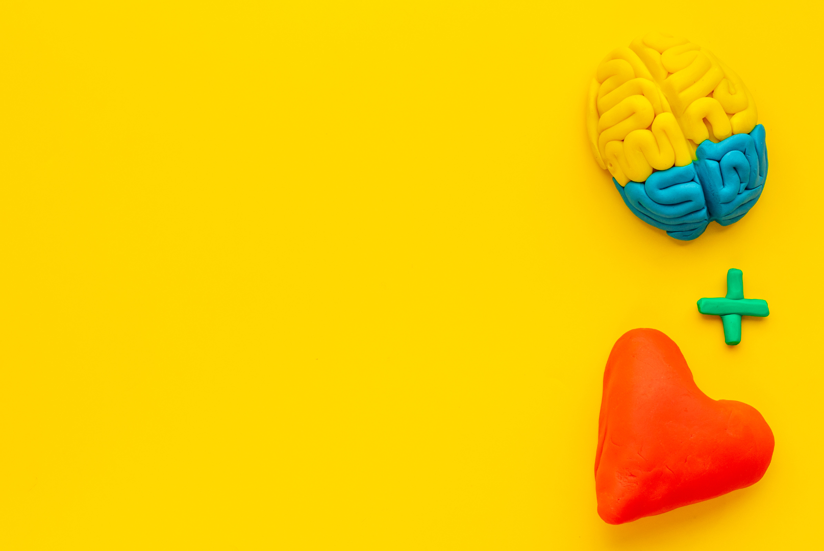 Yellow background with yellow and blue image of a brain. Below the brain is an image of a red heart shape. In between the brain and heart is a plus sign.
